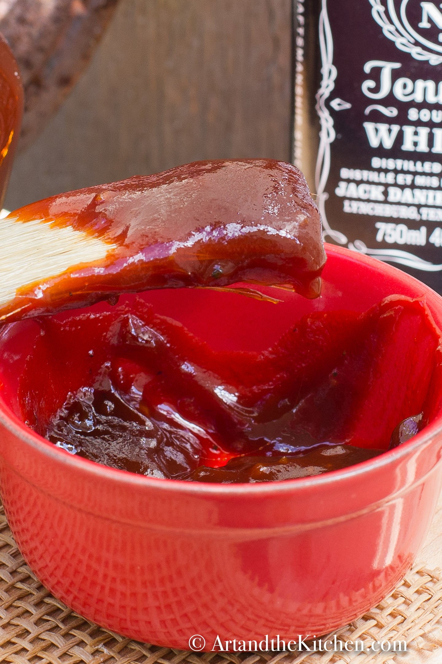 Small red bowl with brush scooping up barbecue sauce. 