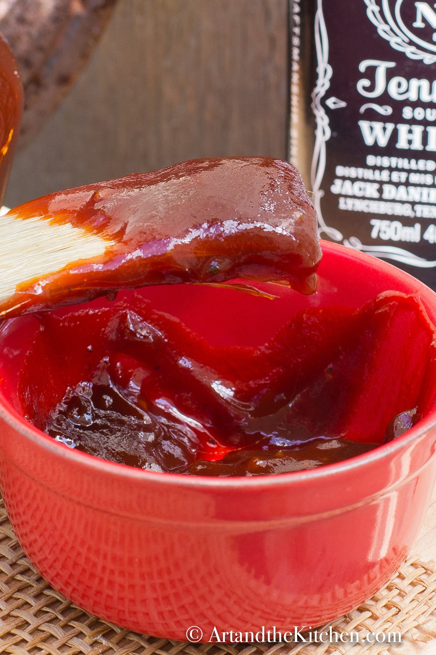 Small red bowl with brush scooping up barbecue sauce.