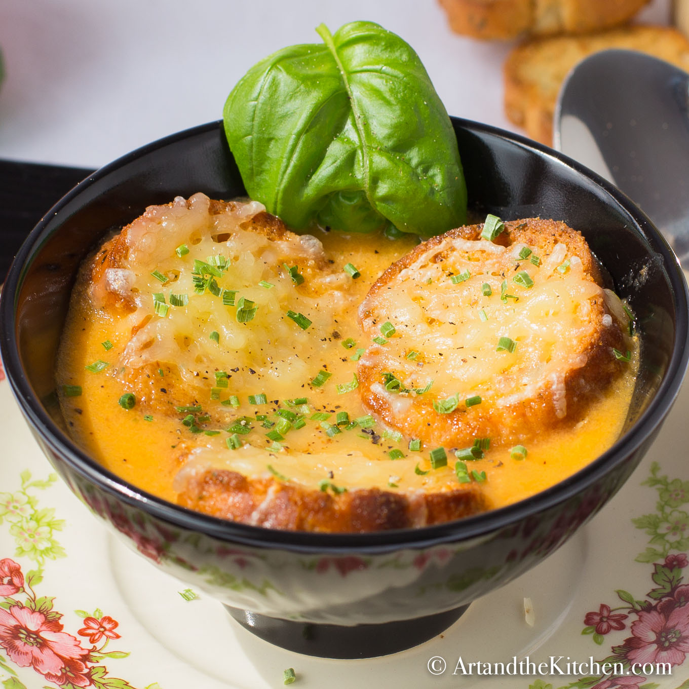 Three crostini with melted cheese crostini on top of tomato soup in black bowl.