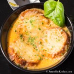 Three crostini with melted cheese on top of tomato soup in black bowl.