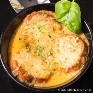 Three crostini with melted cheese on top of tomato soup in black bowl.