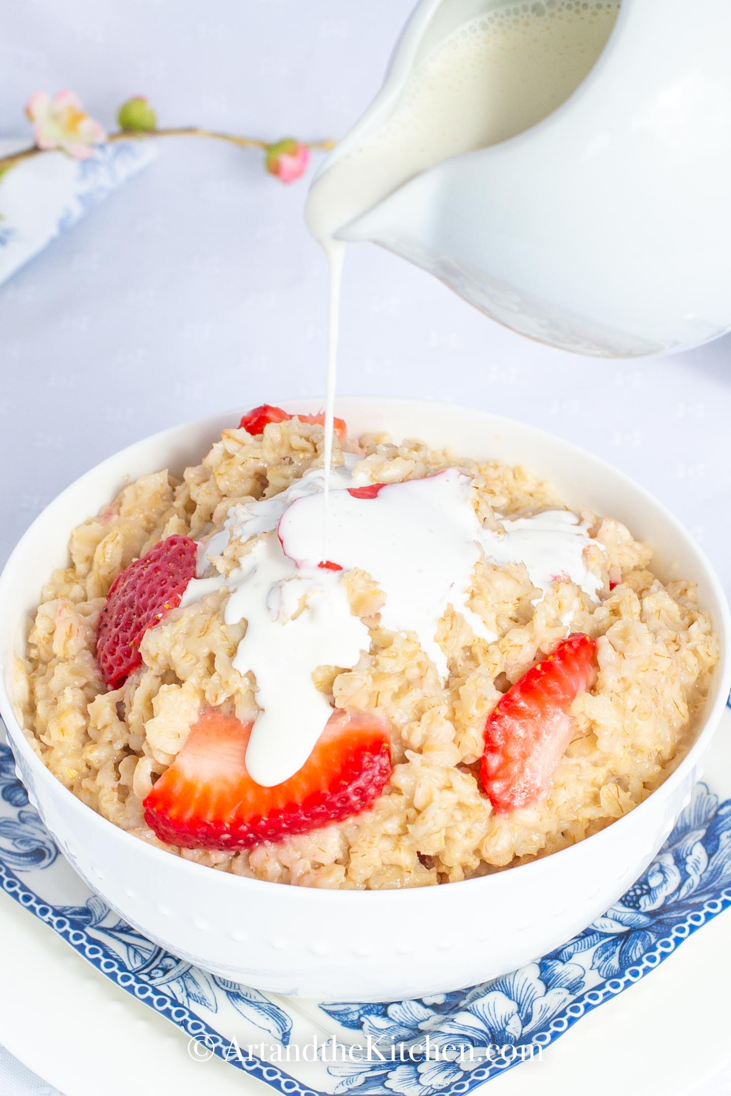 Cream pouring over bowl of oatmeal with strawberries.