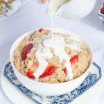 Cream pouring over bowl of oatmeal with strawberries.