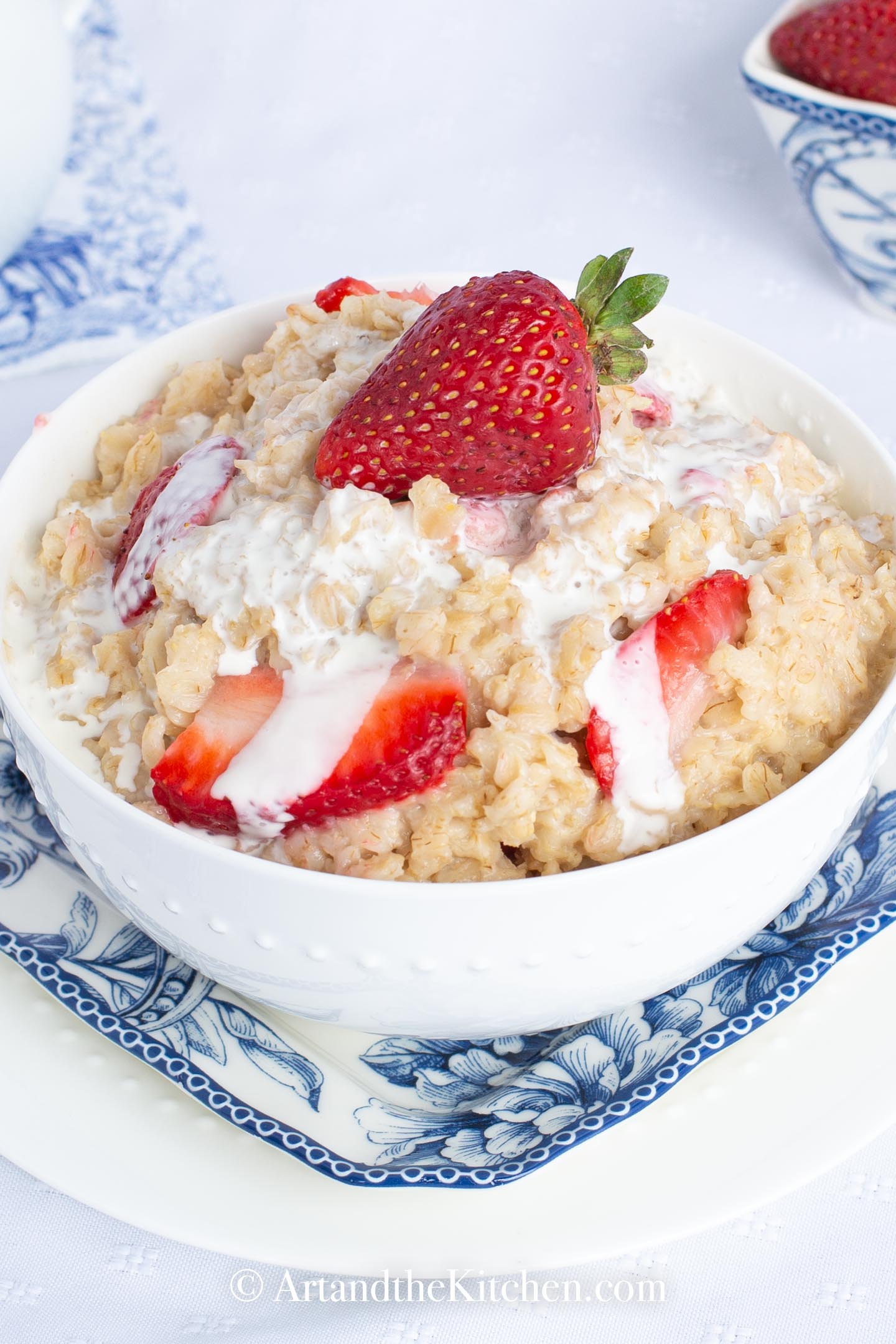White bowl filled with oatmeal topped with fresh strawberries and cream.