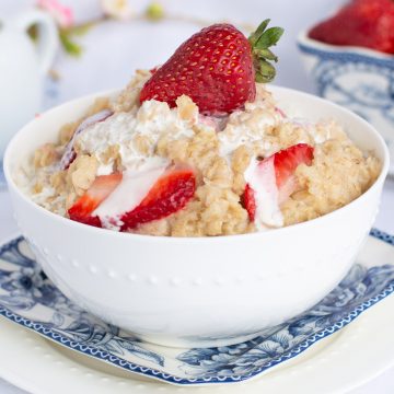 White bowl filled with oatmeal, topped with strawberries and cream.