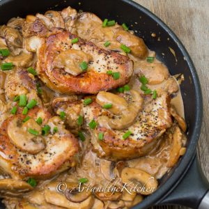 Cast iron frying pan with seared pork chops in a creamy mushroom sauce, garnished with green onion slices.