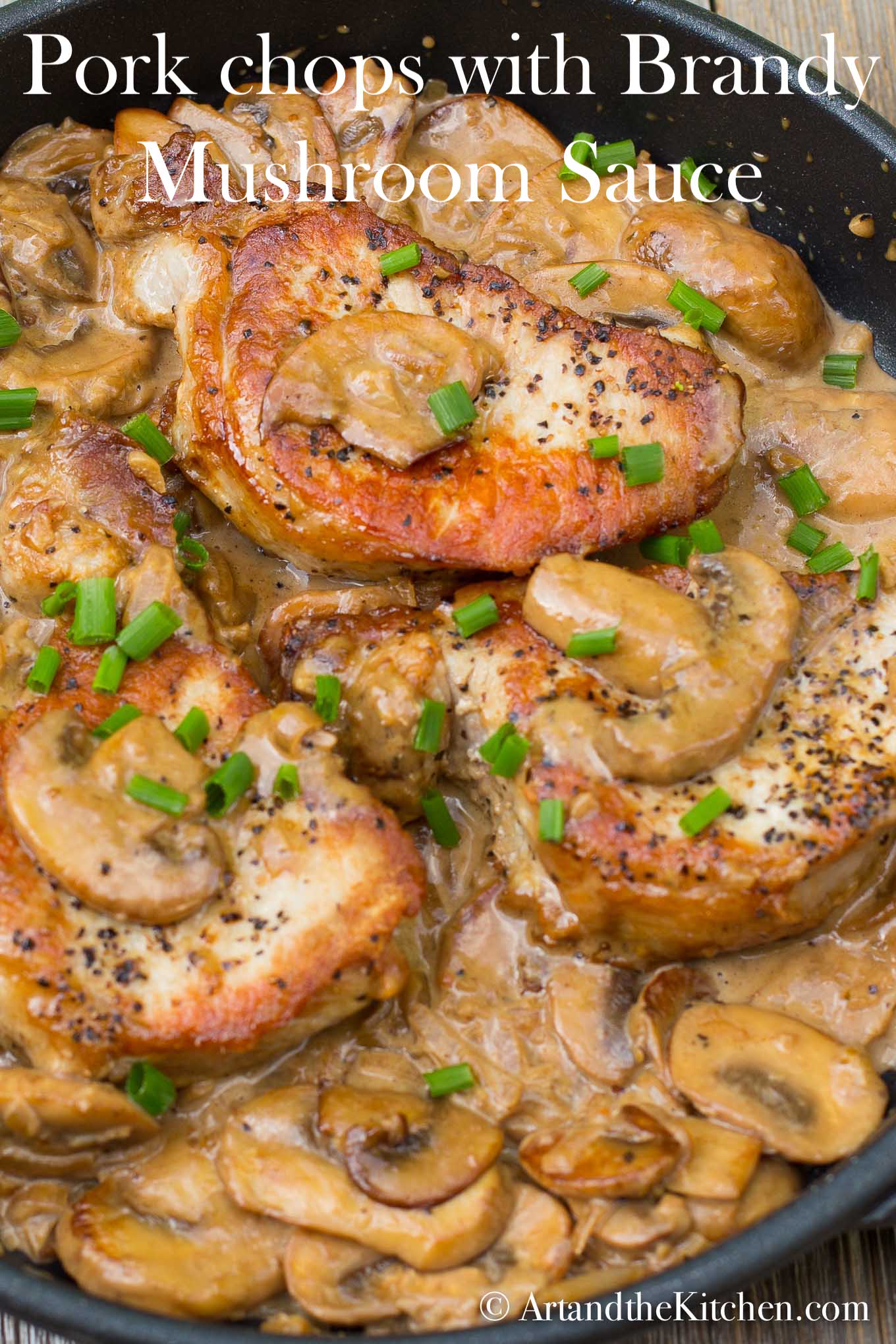 Cast iron frying pan with seared pork chops in a creamy mushroom sauce, garnished with green onion slices. 