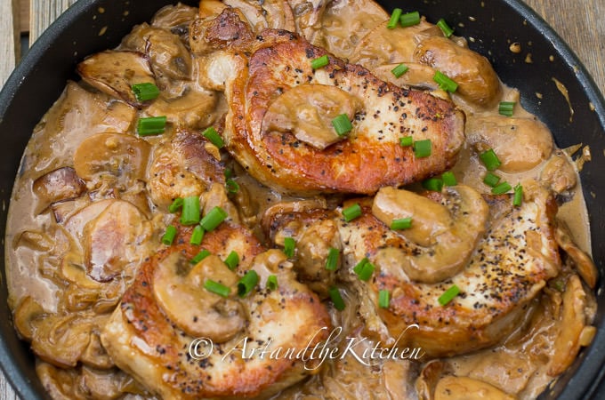 Cast iron frying pan with seared pork chops in a creamy mushroom sauce, garnished with green onion slices. 