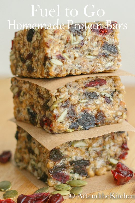 Stack of three homemade protein bars separated with brown parchment paper loaded with seeds and dry fruit