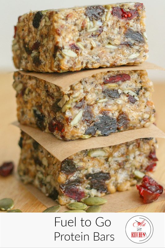 Stack of three homemade protein bars separated with brown parchment paper loaded with seeds and dry fruit