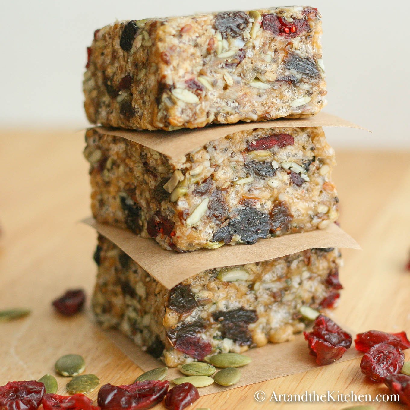 Stack of three homemade protein bars separated with brown parchment paper loaded with seeds and dry fruit