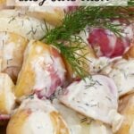 A white bowl of new potatoes coated in a creamy dill sauce garnish with a fresh sprig of dill.