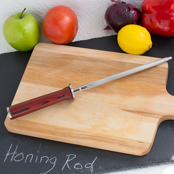 Honing rod on wood cutting board with fruit and vegetables in background.