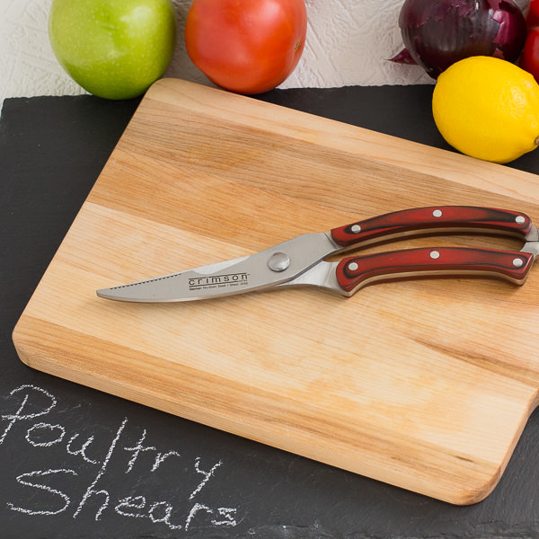 Poultry shears on wood cutting board with fruit and vegetables in background.