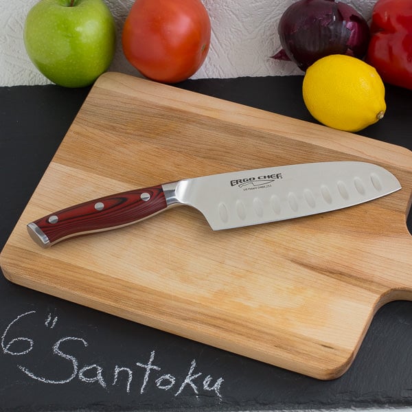 Santoku knife on wood cutting board with fruit and vegetables in background.