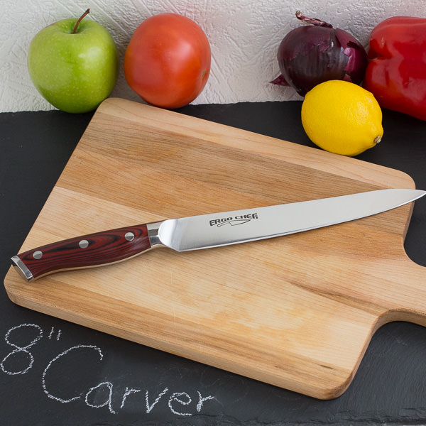 Carving knife on wood cutting board with fruit and vegetables in background.
