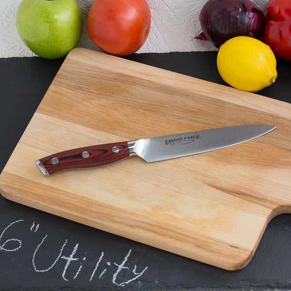 Utility knife on wood cutting board with fruit and vegetables in background.