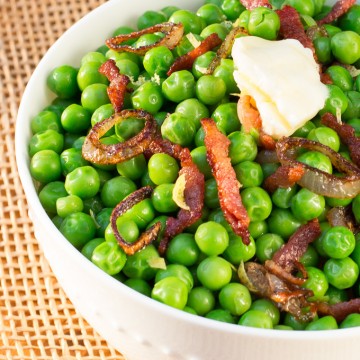 White bowl filled with green peas mixed with bacon and shallots. Topped with a pat of butter.