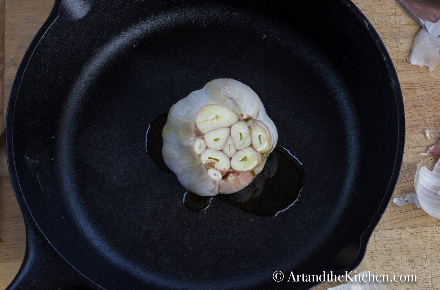 Head of garlic with the top sliced off drizzled with olive oil in a cast iron pan.