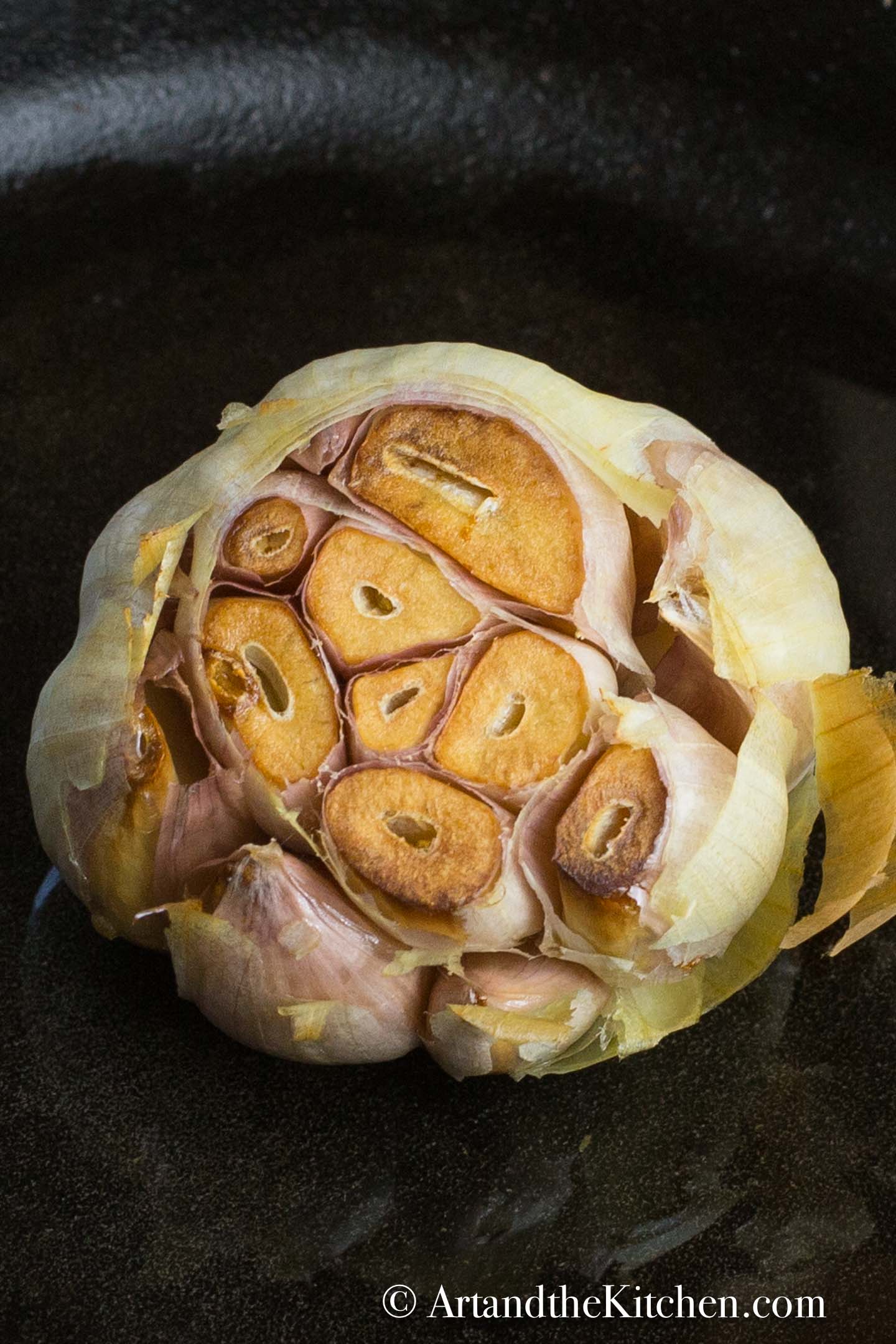 Head of garlic with the top sliced off roasted in a cast iron pan.