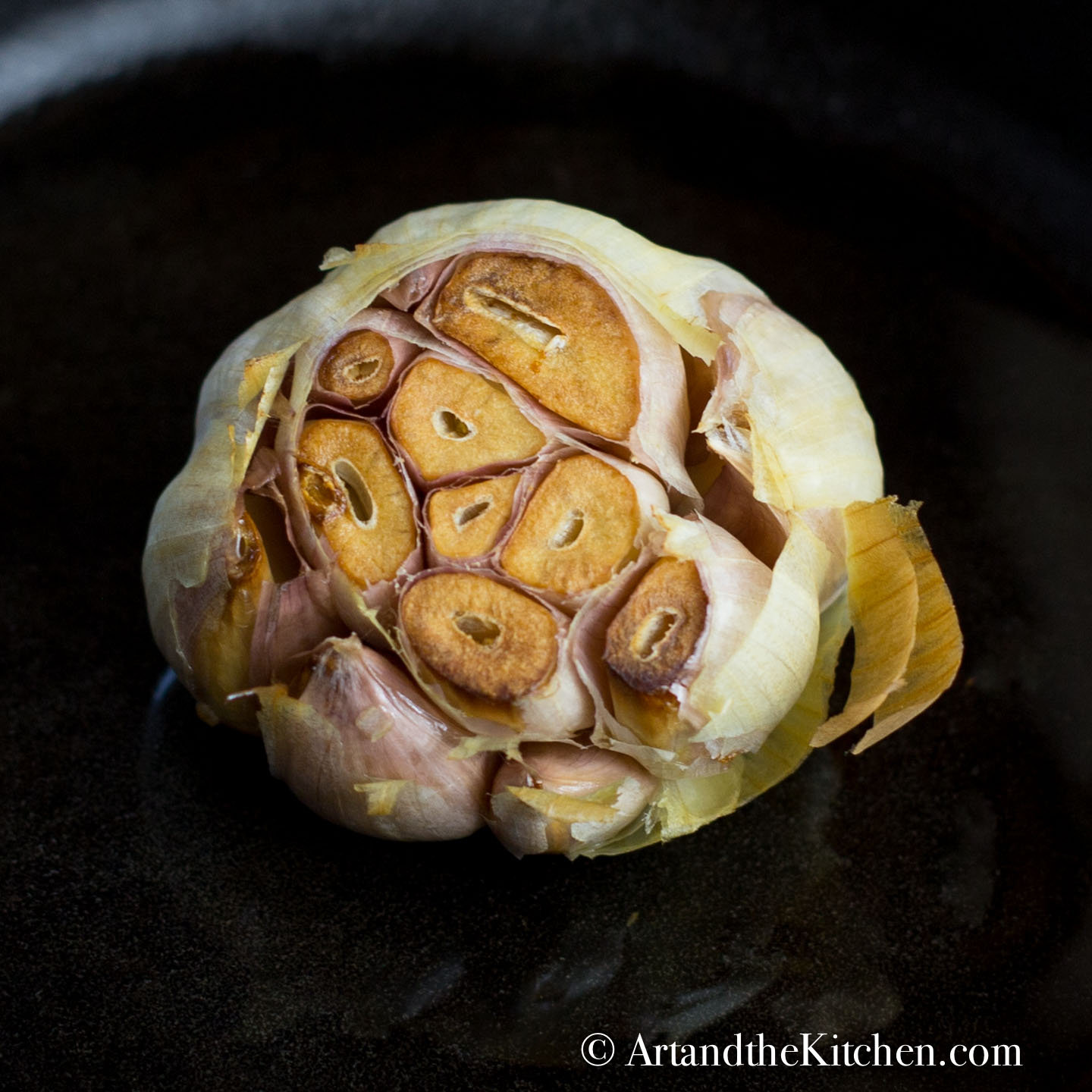 Head of garlic with the top sliced off roasted in a cast iron pan.