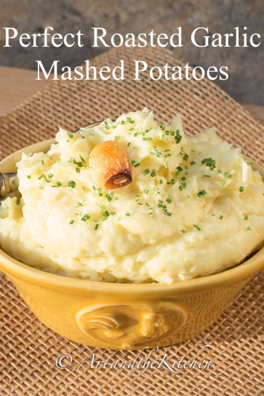 Yellow bowl filled with mashed potatoes garnish with clove of roasted garlic.
