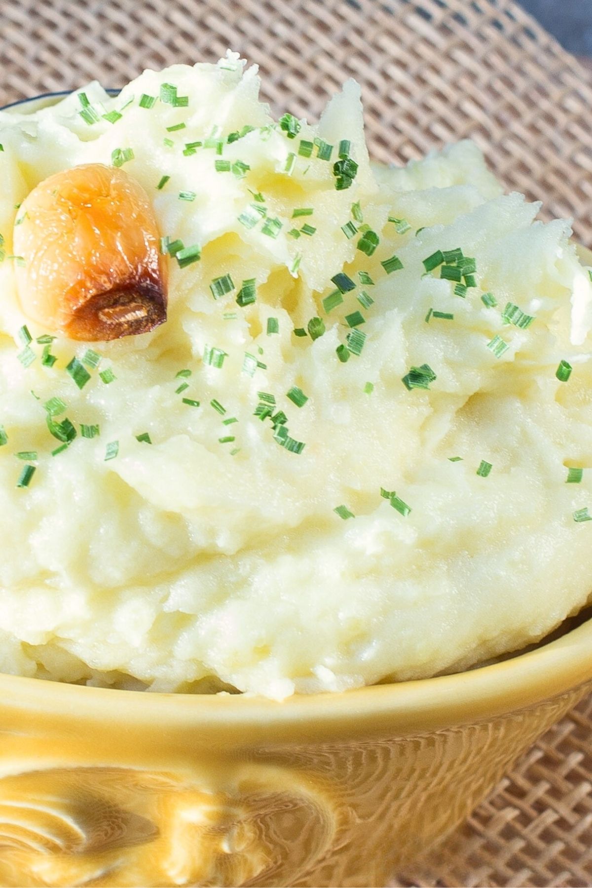 Yellow bowl filled with mashed potatoes, topped with clove of roasted garlic.