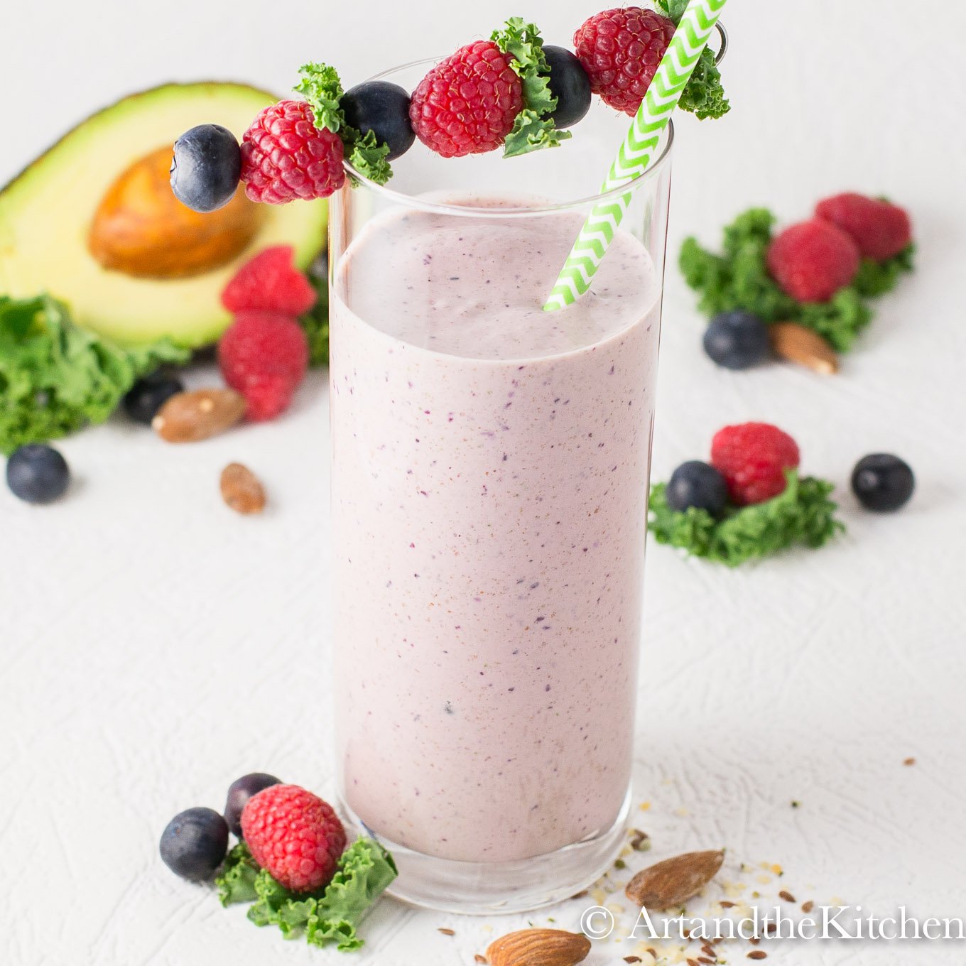 Smoothie in tall glass with green striped straw and fruit garnish.