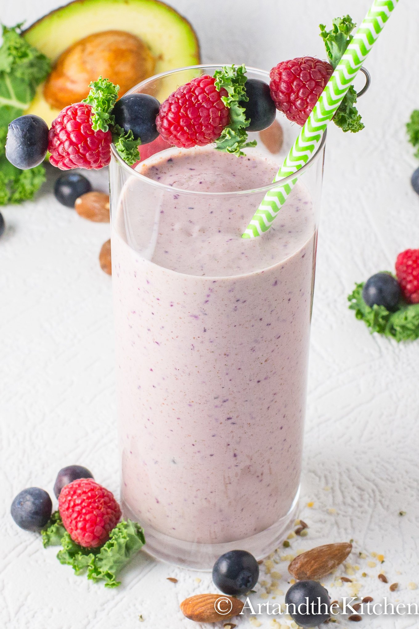 Smoothie in tall glass with berries, nuts and avocado in background