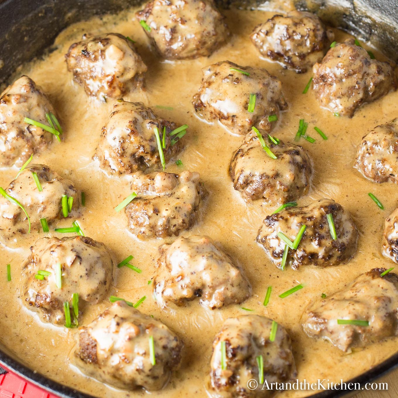 Meatballs simmering in a creamy sauce in a cast iron skillet, garnished with chives.