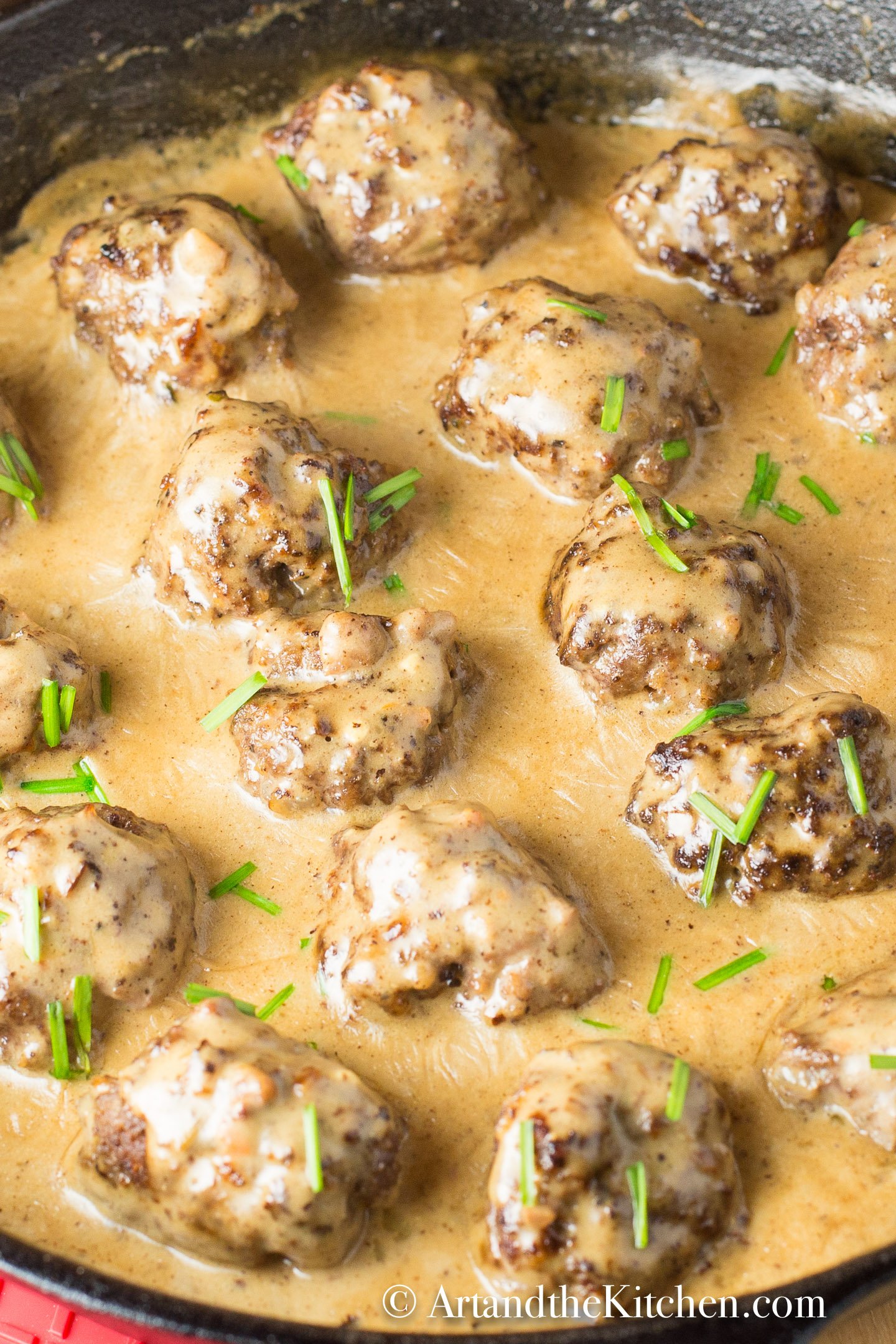  Meatballs simmering in a creamy sauce in a cast iron skillet, garnished with chives.