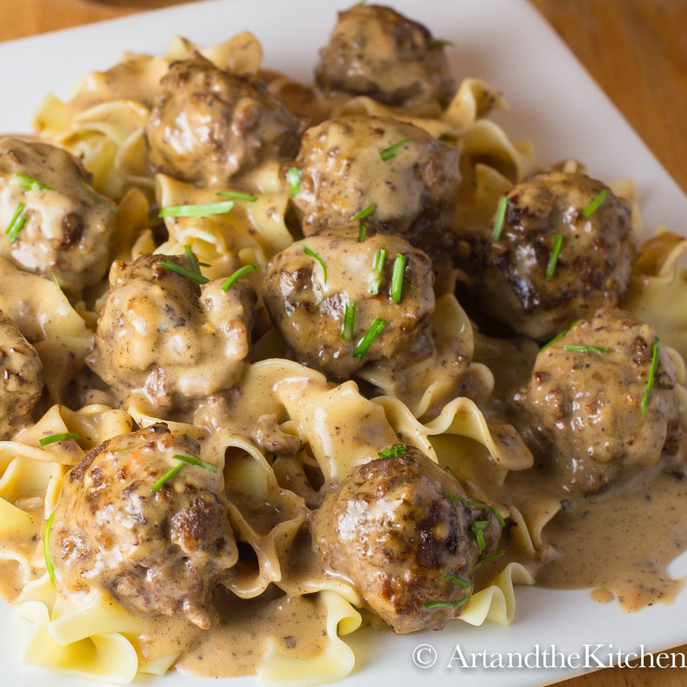 Broad noodles topped with in a creamy ground beef sauce on a white plate.