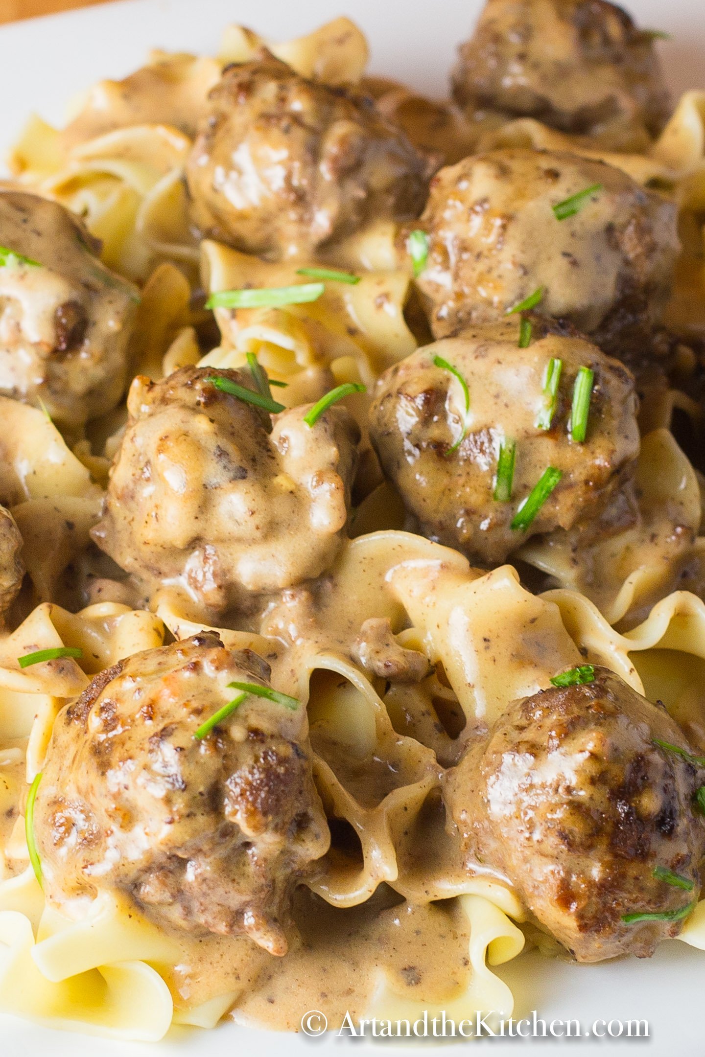 Broad noodles topped with meatballs in a creamy sauce on a white plate.