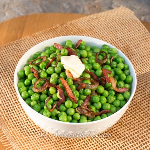 White bowl filled with green peas mixed with bacon and shallots. Topped with a pat of butter.