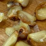 Cloves of roasted garlic on a wood cutting board.