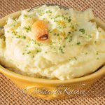 Yellow bowl filled with mashed potatoes, topped with clove of roasted garlic.