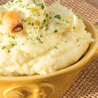 Yellow bowl filled with mashed potatoes, topped with clove of roasted garlic.