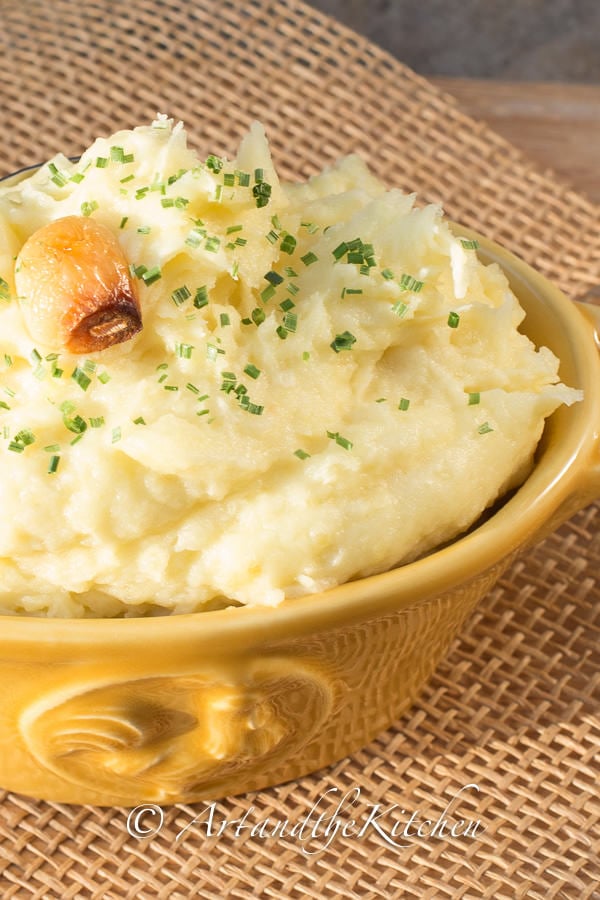 Yellow bowl filled with mashed potatoes, topped with clove of roasted garlic.
