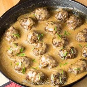 Meatballs simmering in a creamy sauce in a cast iron skillet, garnished with chives.