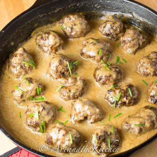 Meatballs simmering in a creamy sauce in a cast iron skillet, garnished with chives.