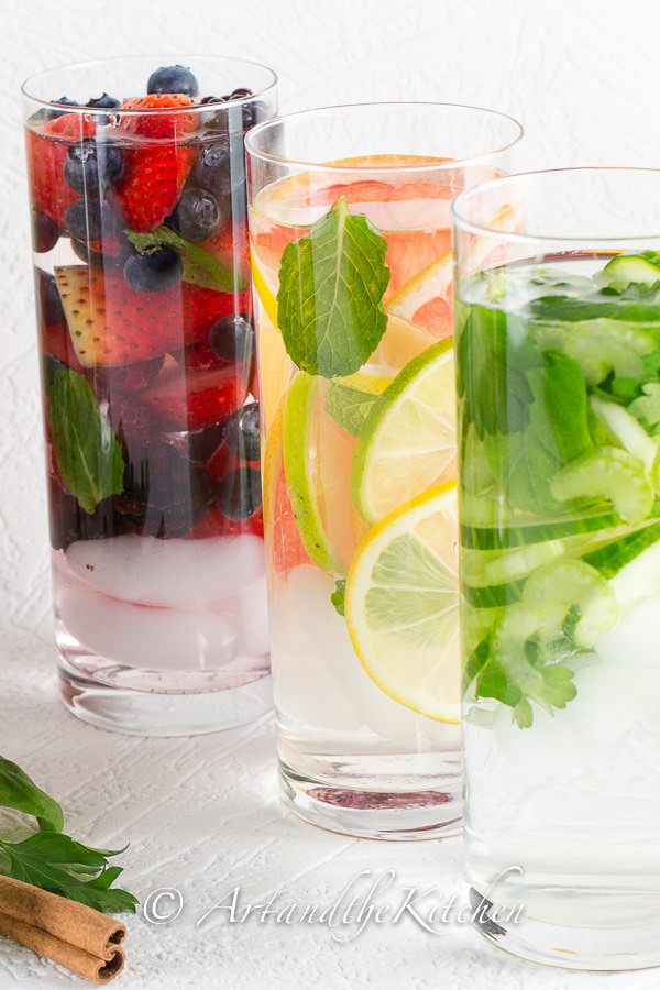 Three tall glasses filled with water and fresh fruit.