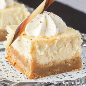 Slice of eggnog cheese with brownie crust. Decorated with a dollop of whipped cream and chocolate stick.