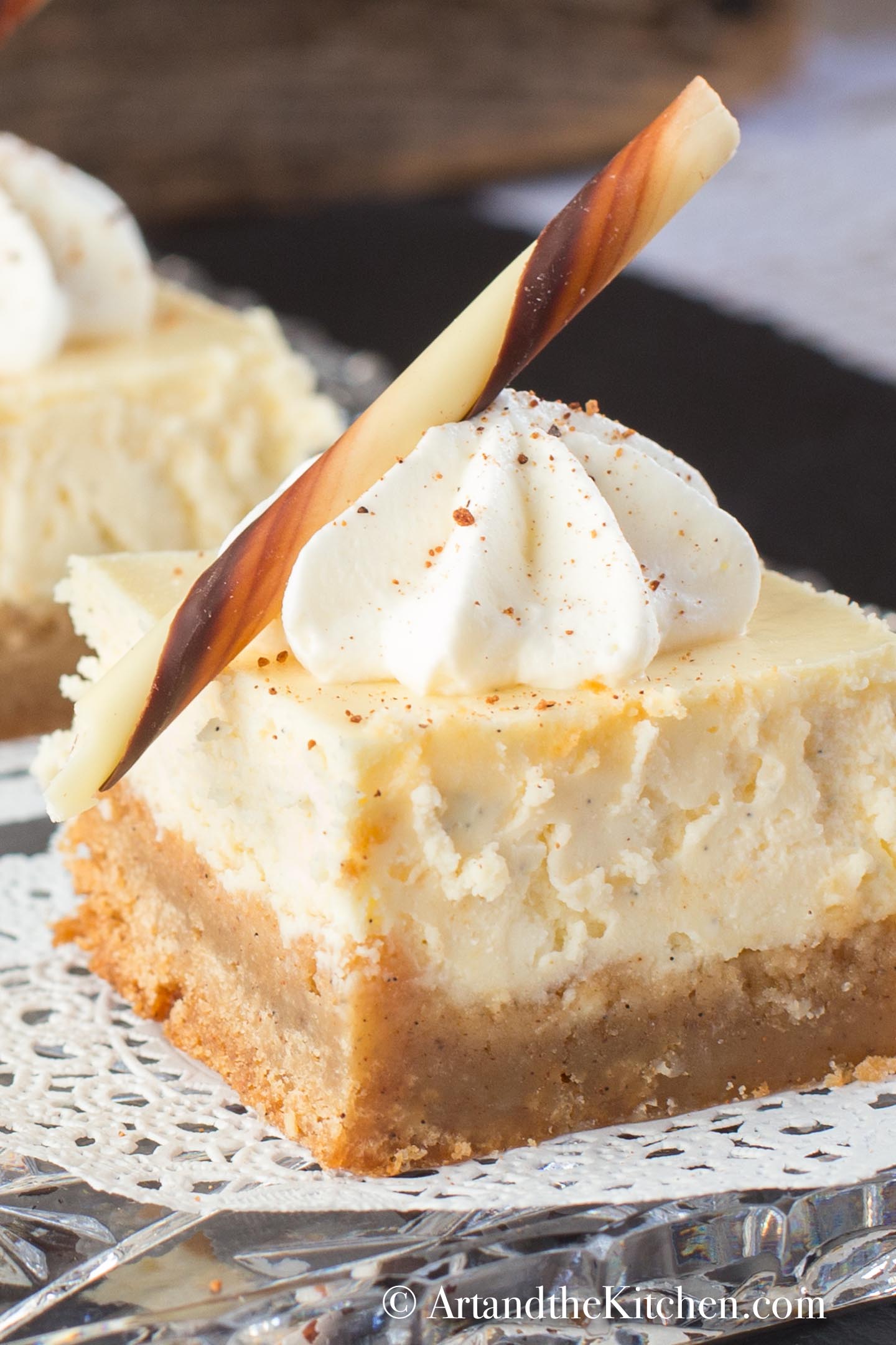 Slice of eggnog cheese with brownie crust. Decorated with a dollop of whipped cream and chocolate stick.