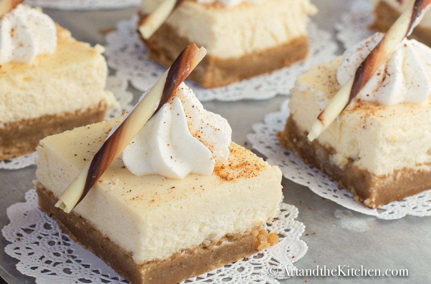 Serving tray filled with cheesecake squares on paper dollies. Garnished with dollop of whipped cream and chocolate rod.