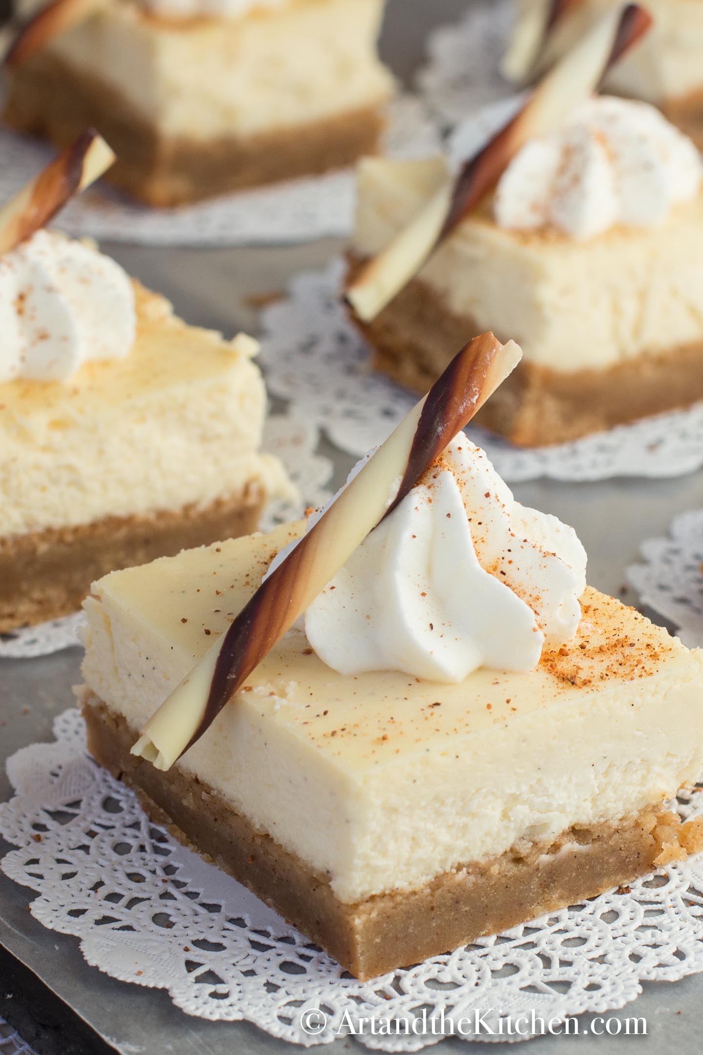 Squares of cheesecake on white paper dollies. Decorated with a dollop of whipped cream and chocolate stick.