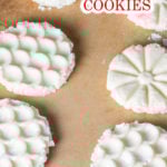 Six unbaked shortbread cookies with intricate patterns rest on a parchment-lined baking sheet.