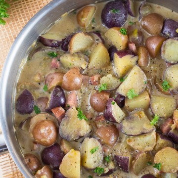 Cubes of potatoes and ham in creamy sauce cooking in stainless steel pan.