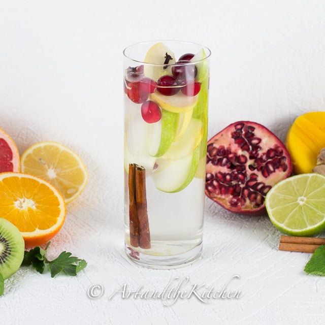 Tall glass of water with apple slices, cranberries and cinnamon stick.