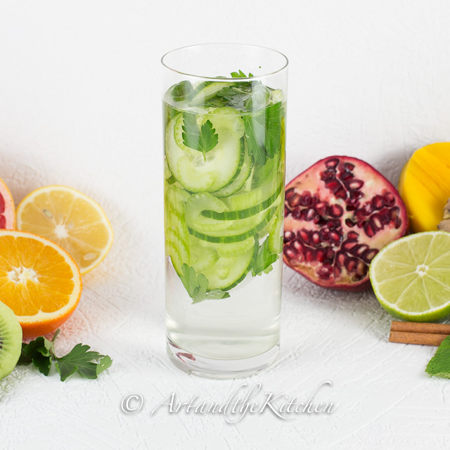 Tall glass of water with cucumber, celery and parsley slices.