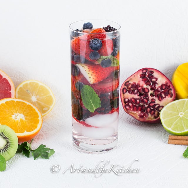 Tall glass of water with strawberries, blackberries, blueberries and mint.